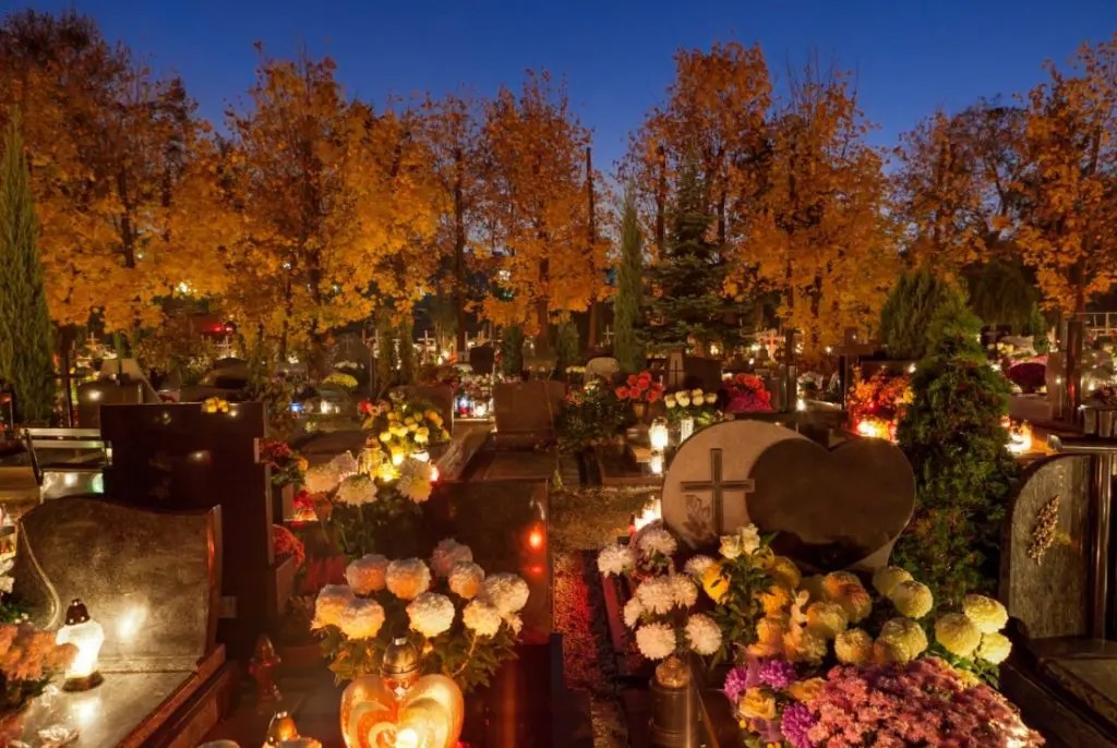 Morminte împodobite cu flori și lumânări într-un cimitir, foto ilustrativă